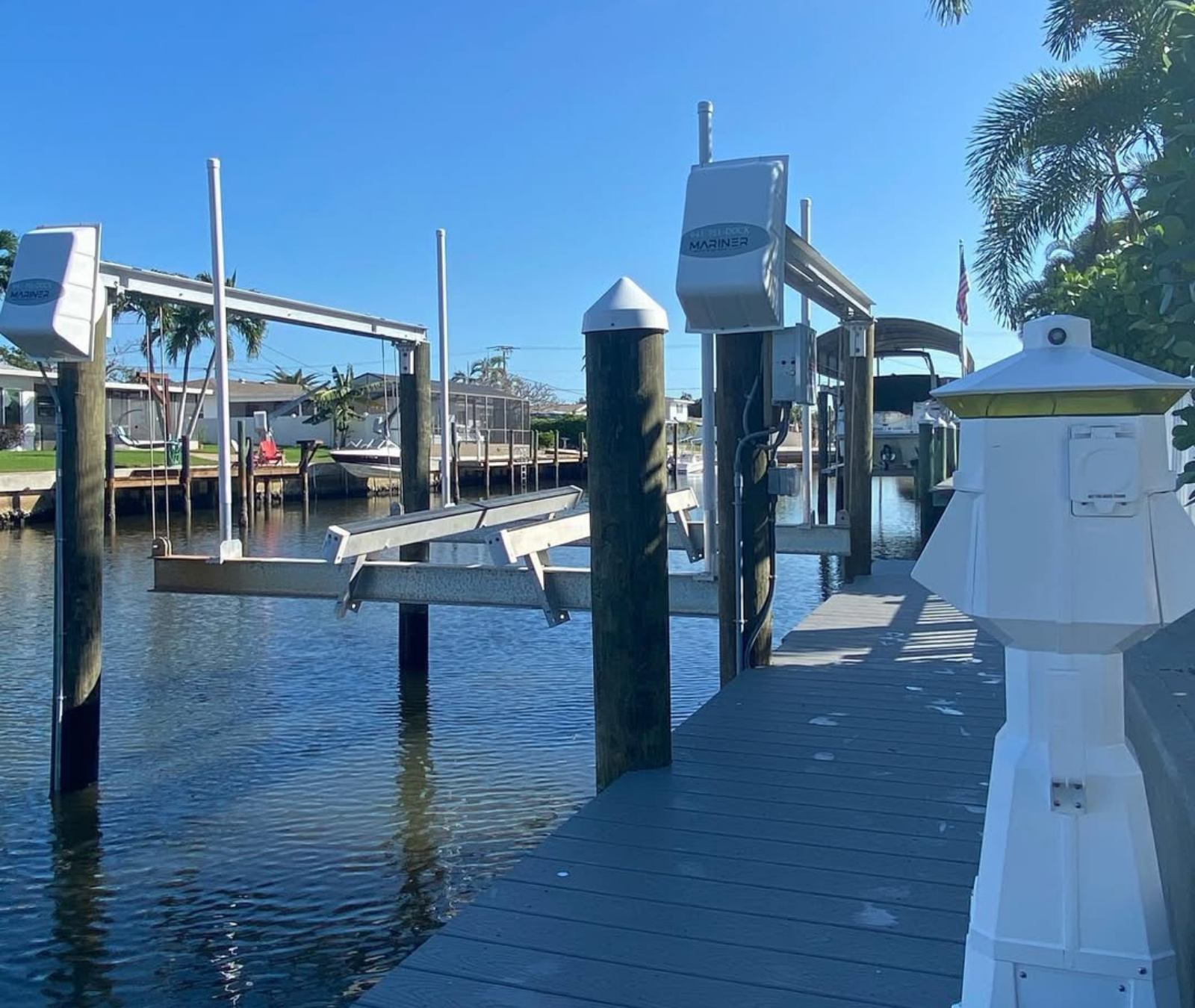 A boat lift stands above a canal next to a wooden dock on a sunny day.