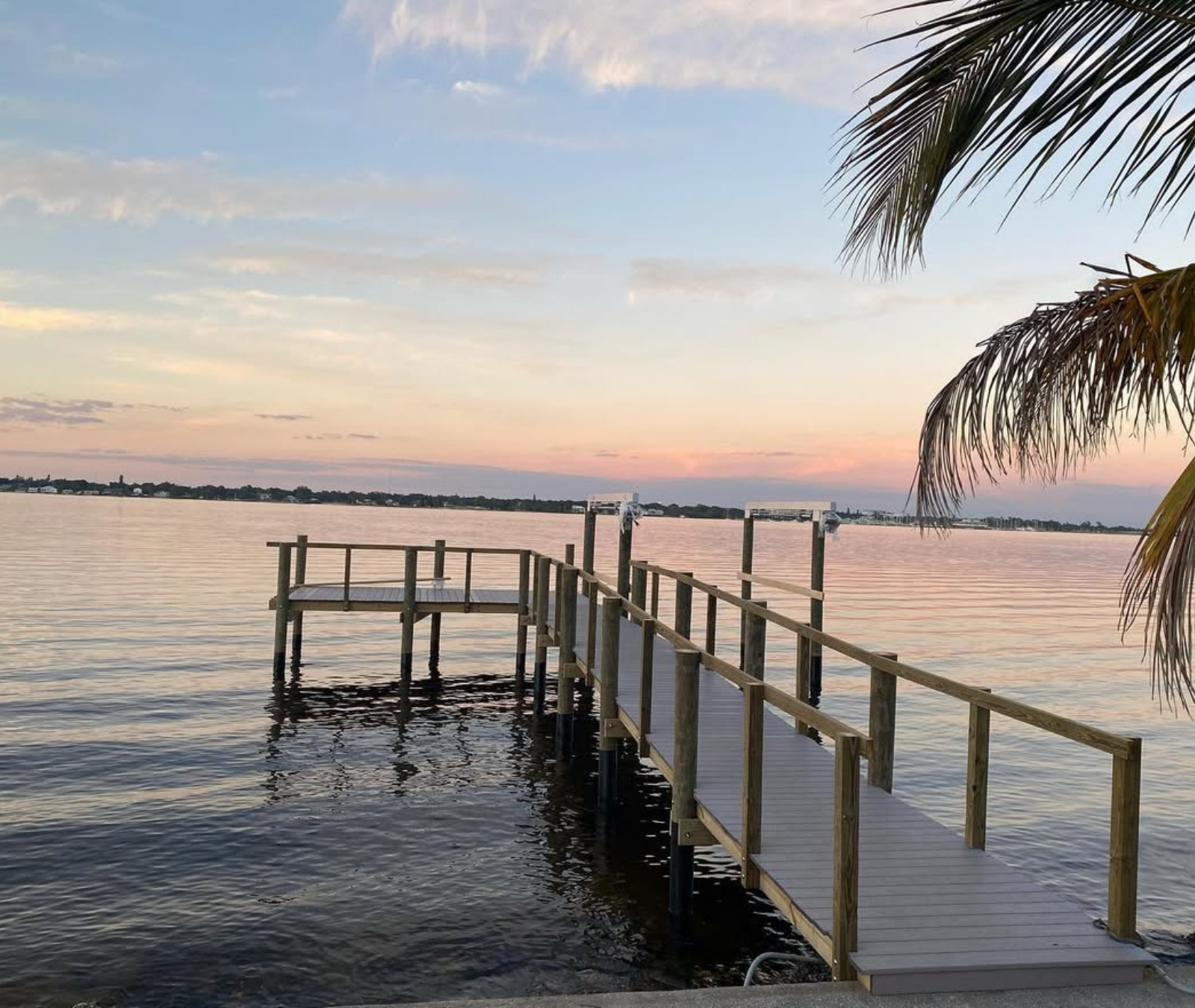A wooden pier extends into a calm, wide body of water under a soft, pastel-colored sunset.