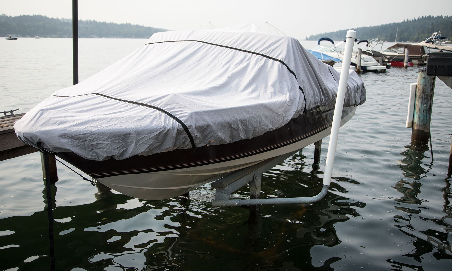 Covered boat on a lift in calm marina water, with dock posts and cloudy shoreline in the background