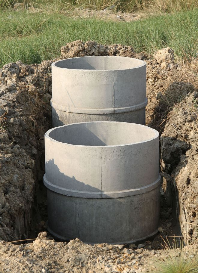 Two stacked concrete drainage pipes in a dirt excavation, with grass around the edges.
