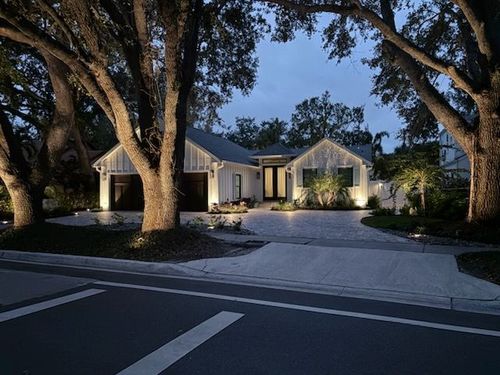 House at dusk with warm exterior lights, large oak trees, and a curved driveway in front