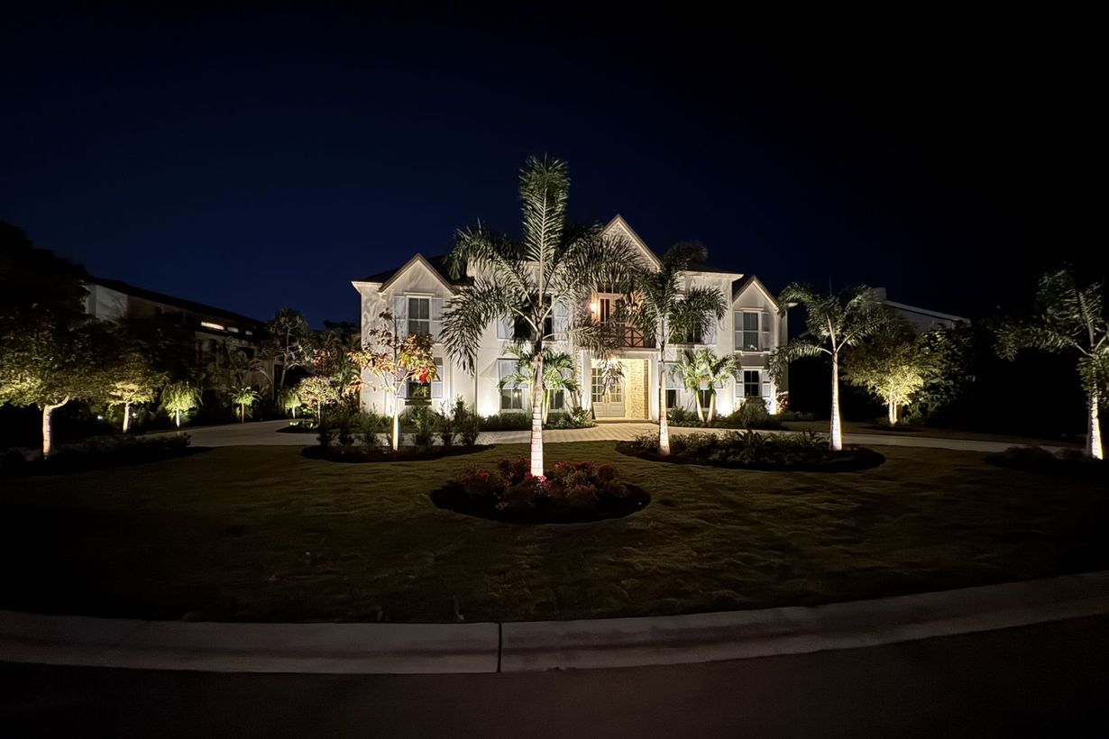 Illuminated large suburban house at night with landscaped front yard and palm trees