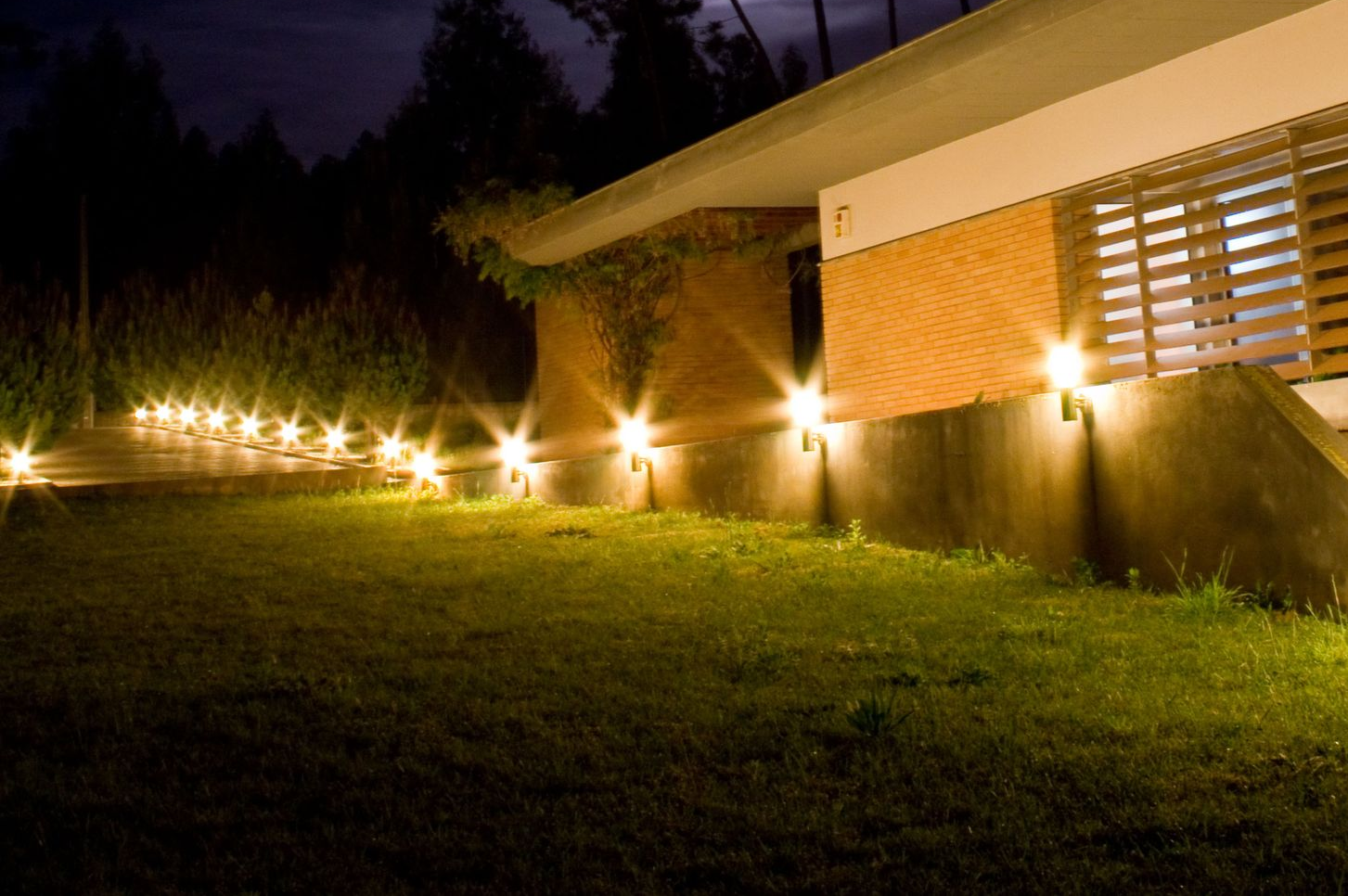 Lit walkway lights illuminating a grassy yard beside a brick house at night