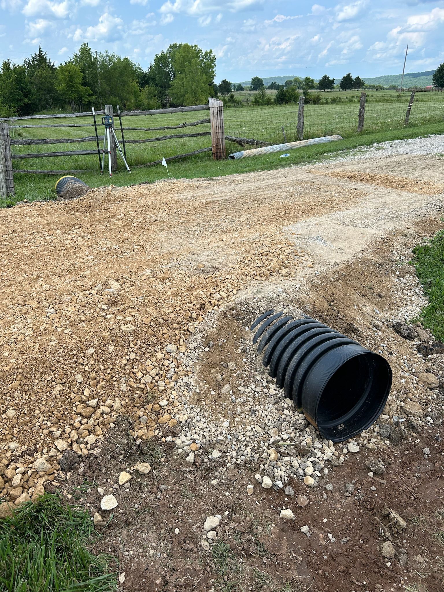 A black pipe is laying on the ground next to a gravel road.