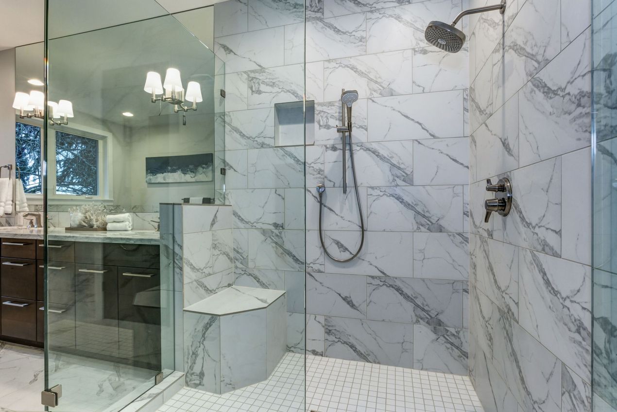 Spacious marble-tiled shower with glass doors, a bench, and multiple showerheads in a modern bathroom.
