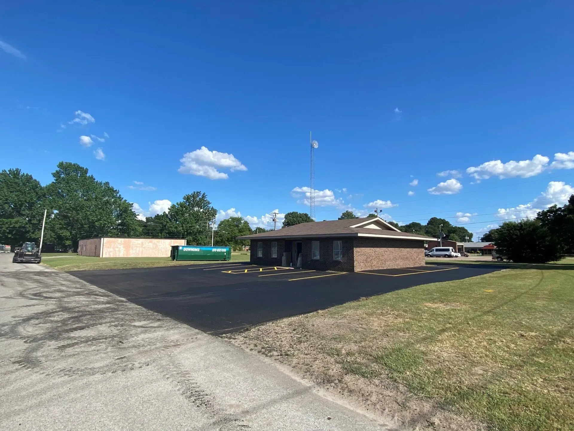 Low brick building with a green dumpster beside an empty paved lot under a blue sky.