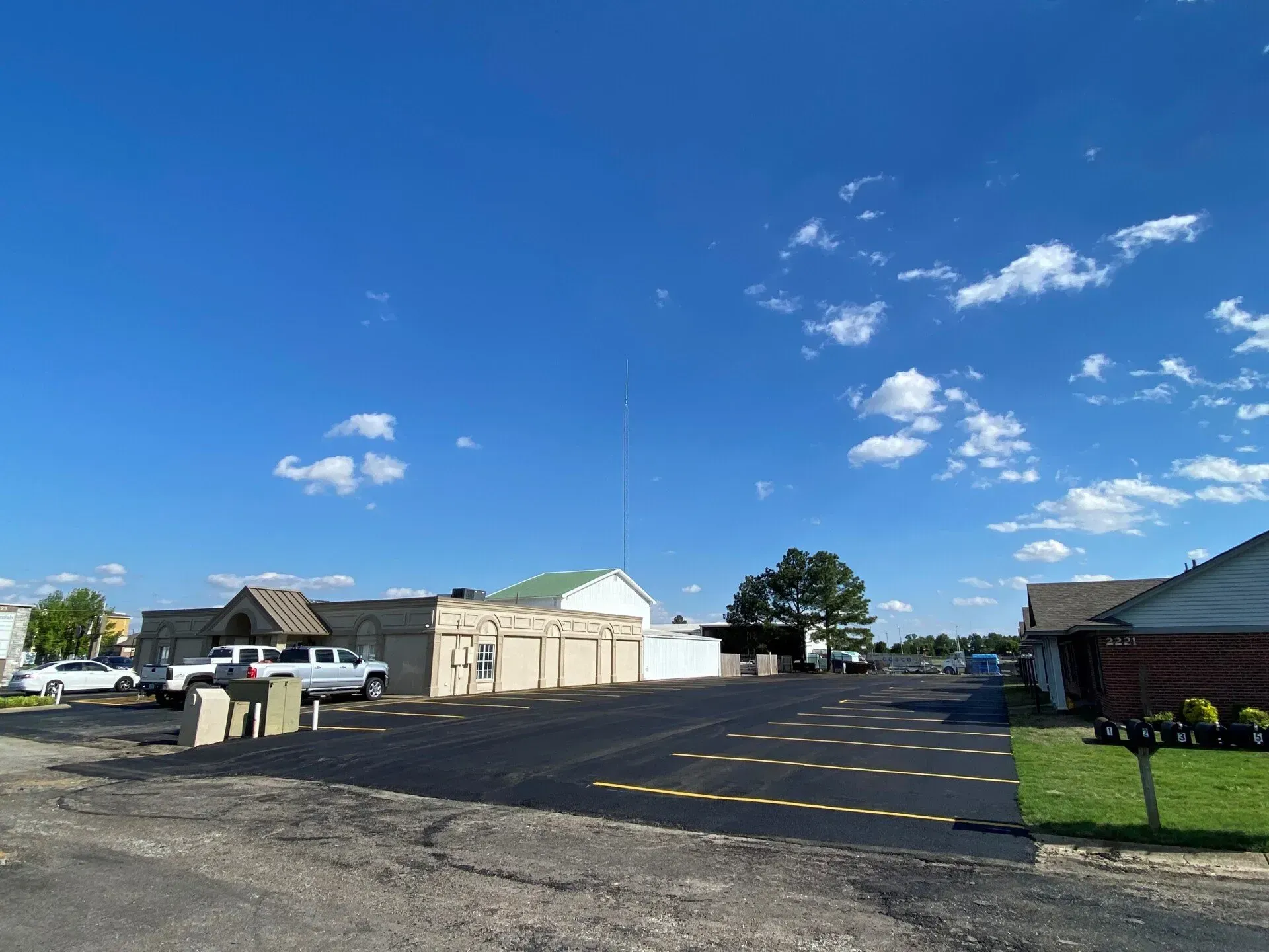 Empty parking lot beside houses under a bright blue sky with scattered clouds