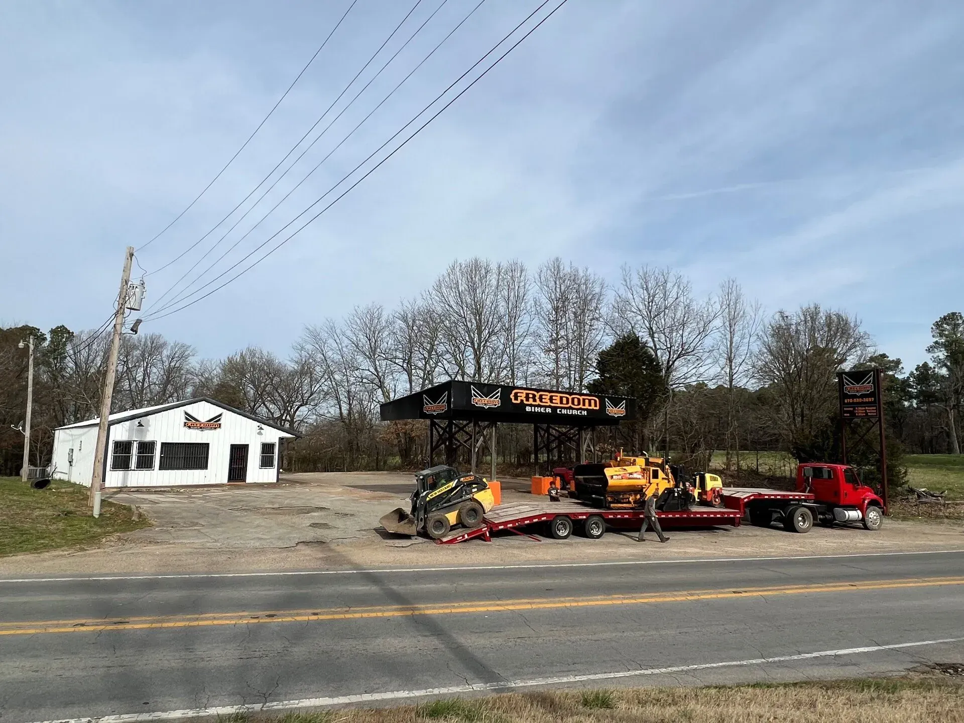 Roadside auto salvage yard with wrecked cars and a red tow truck beside a white building