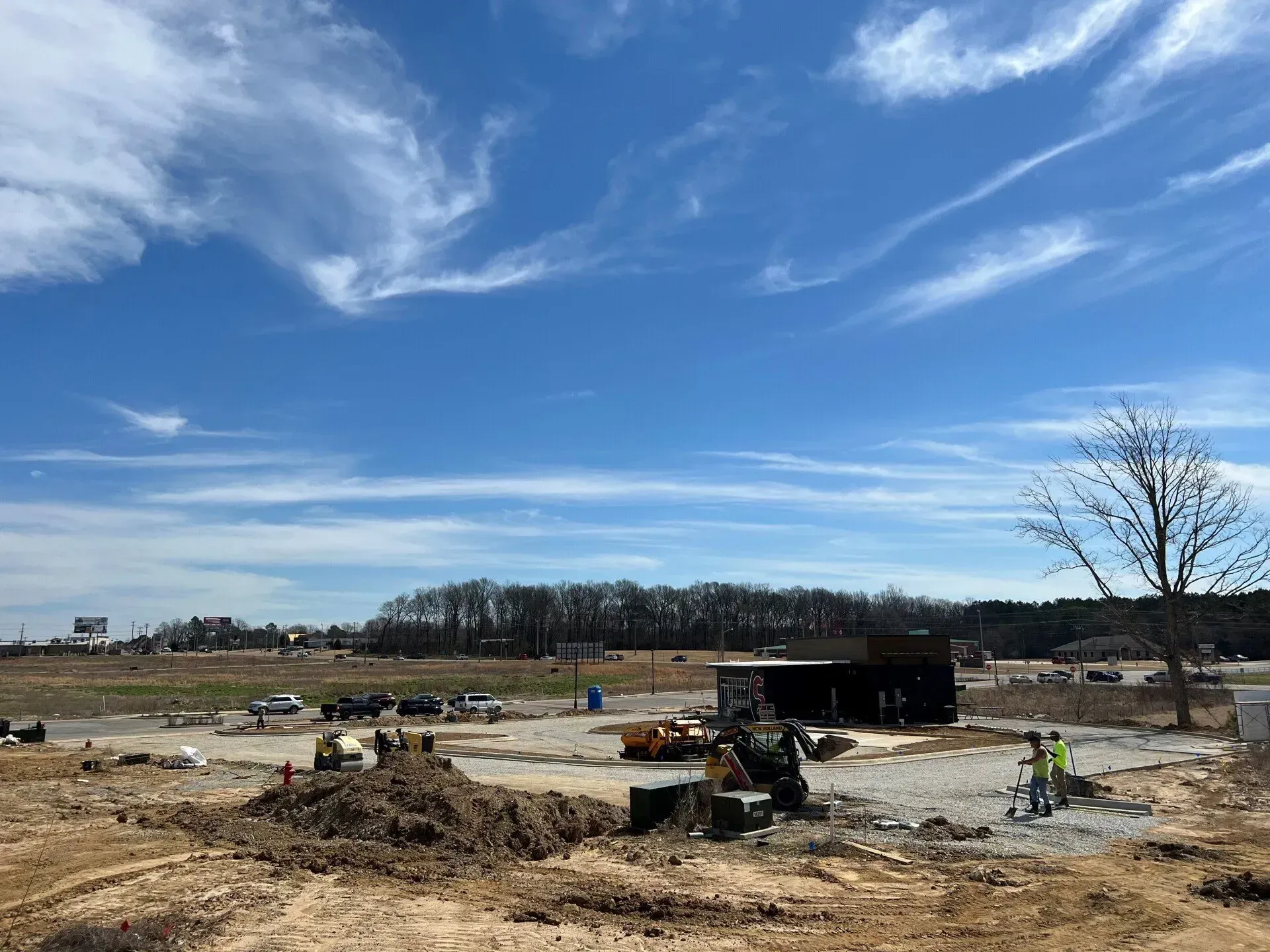Construction site with heavy equipment and workers under a blue, cloudy sky