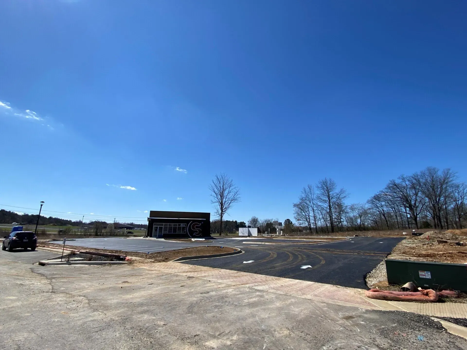 Empty gravel lot with a small black building, blue sky, and construction materials scattered around