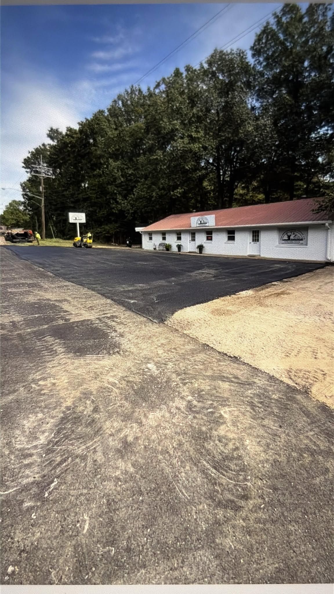 Gravel parking lot beside a small white building with a red roof and trees in the background