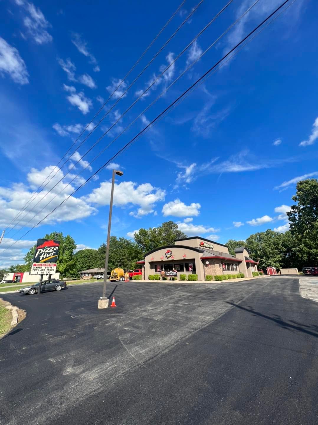 Commercial building with red awning beside a freshly paved parking lot under a blue sky