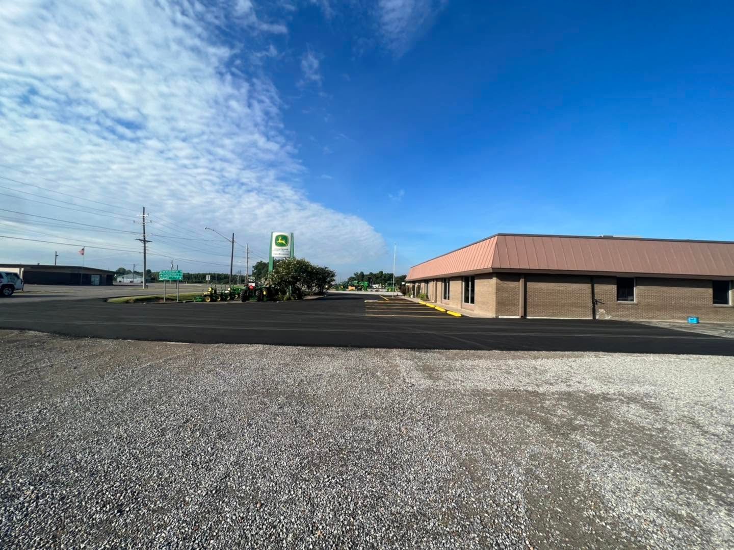 Parking lot beside a tan building under a bright blue sky with clouds