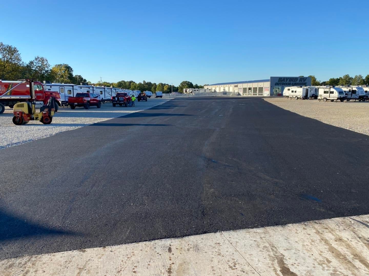 Large freshly paved lot with trucks and equipment along the sides under a clear blue sky
