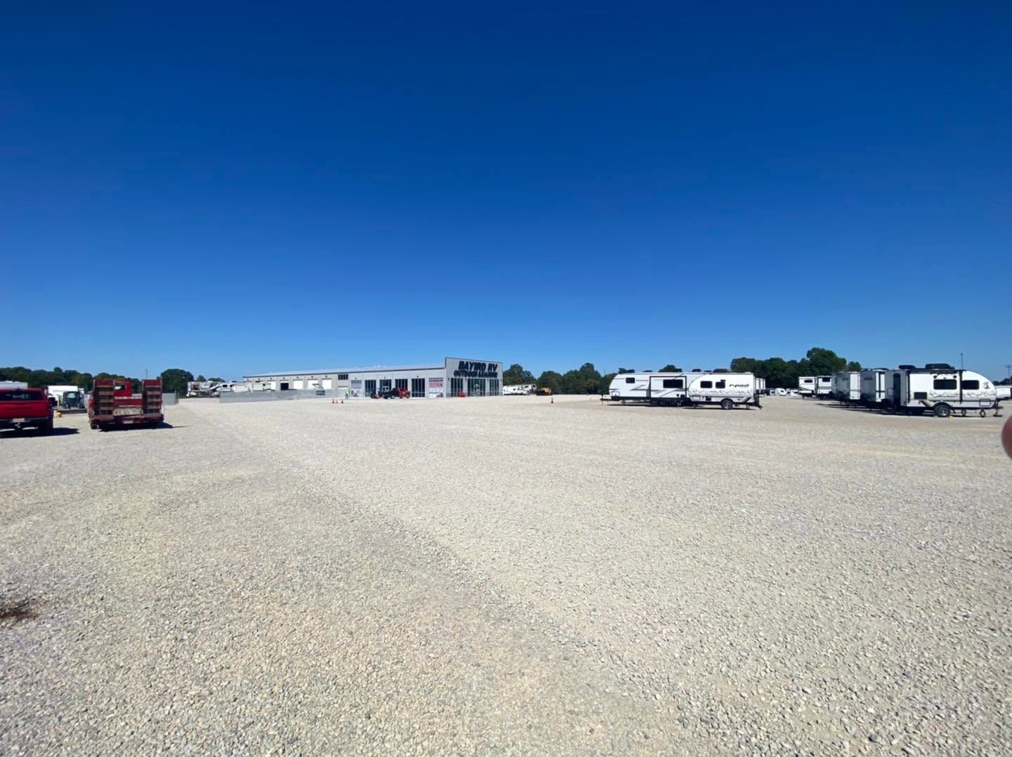 Wide gravel lot with parked RVs and trucks under a clear blue sky