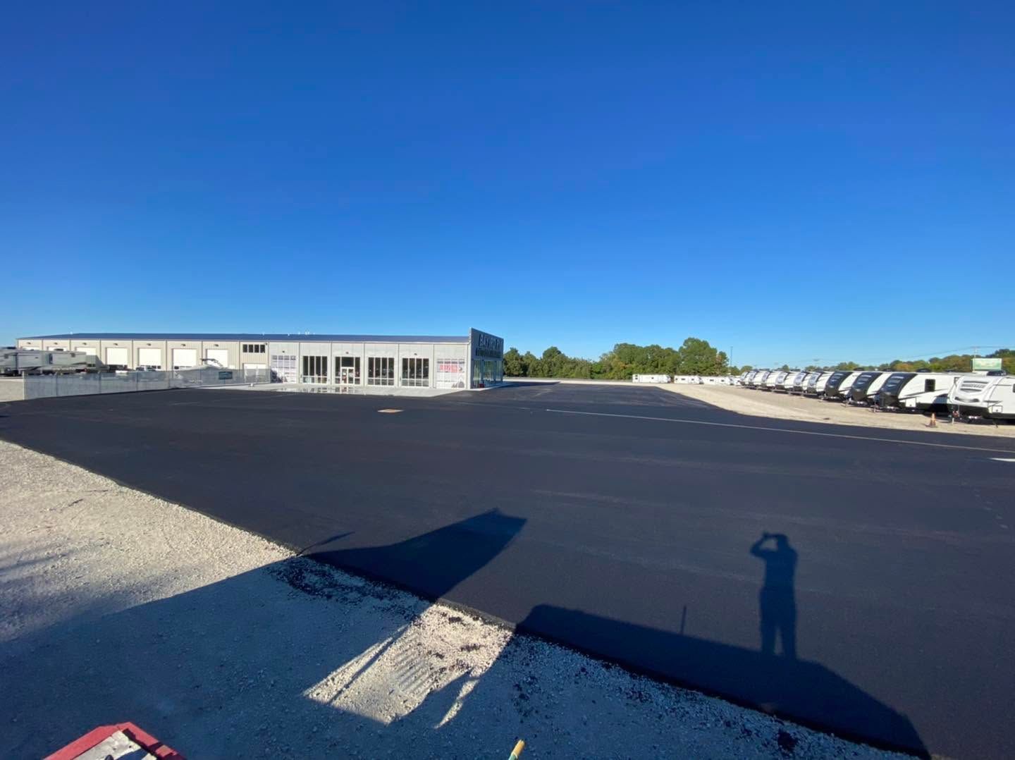 Large paved parking lot beside industrial buildings, with parked trucks under a clear blue sky.