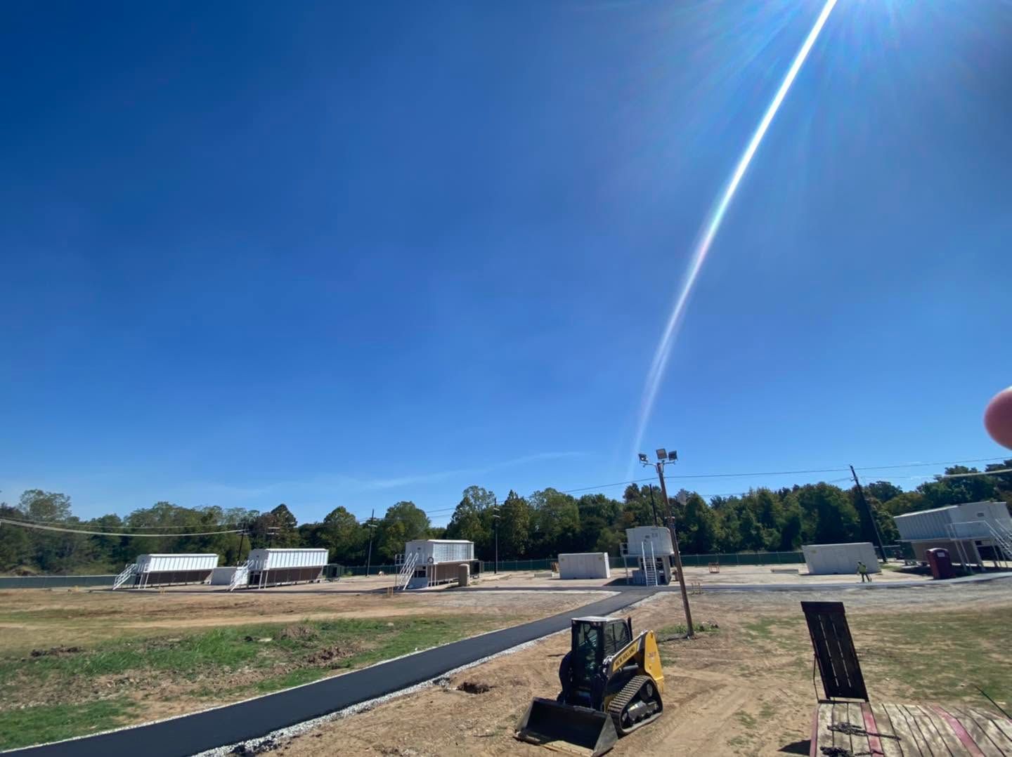 Launch pad with rocket plume arcing into a clear blue sky over a rural field