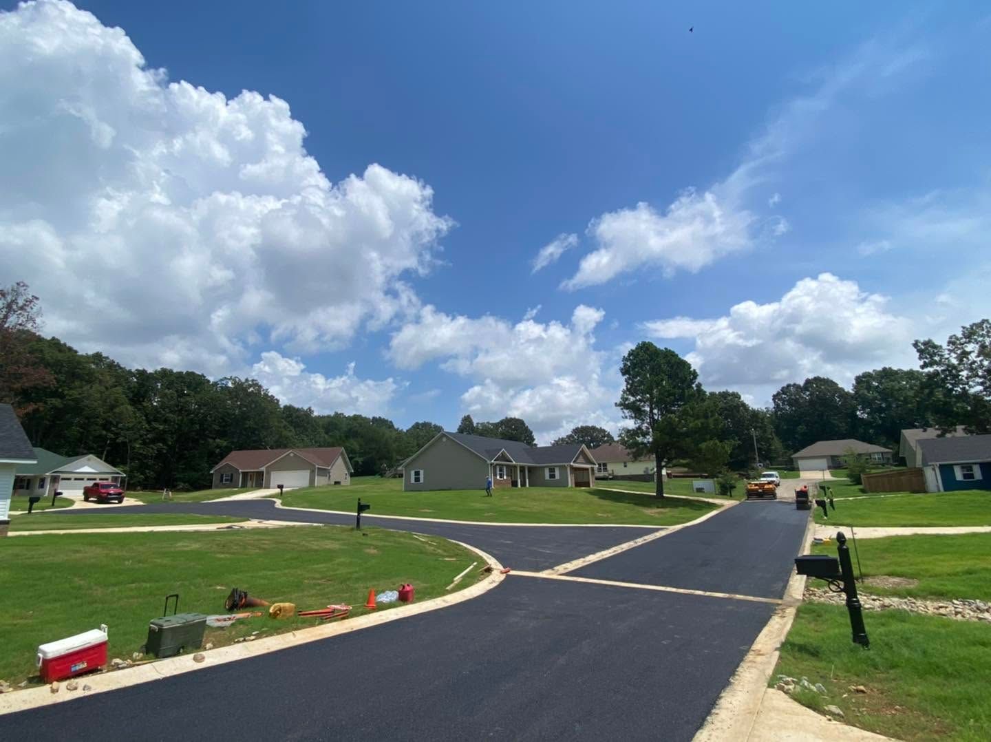 New suburban neighborhood with curving paved road, green lawns, and houses under a blue sky with clouds