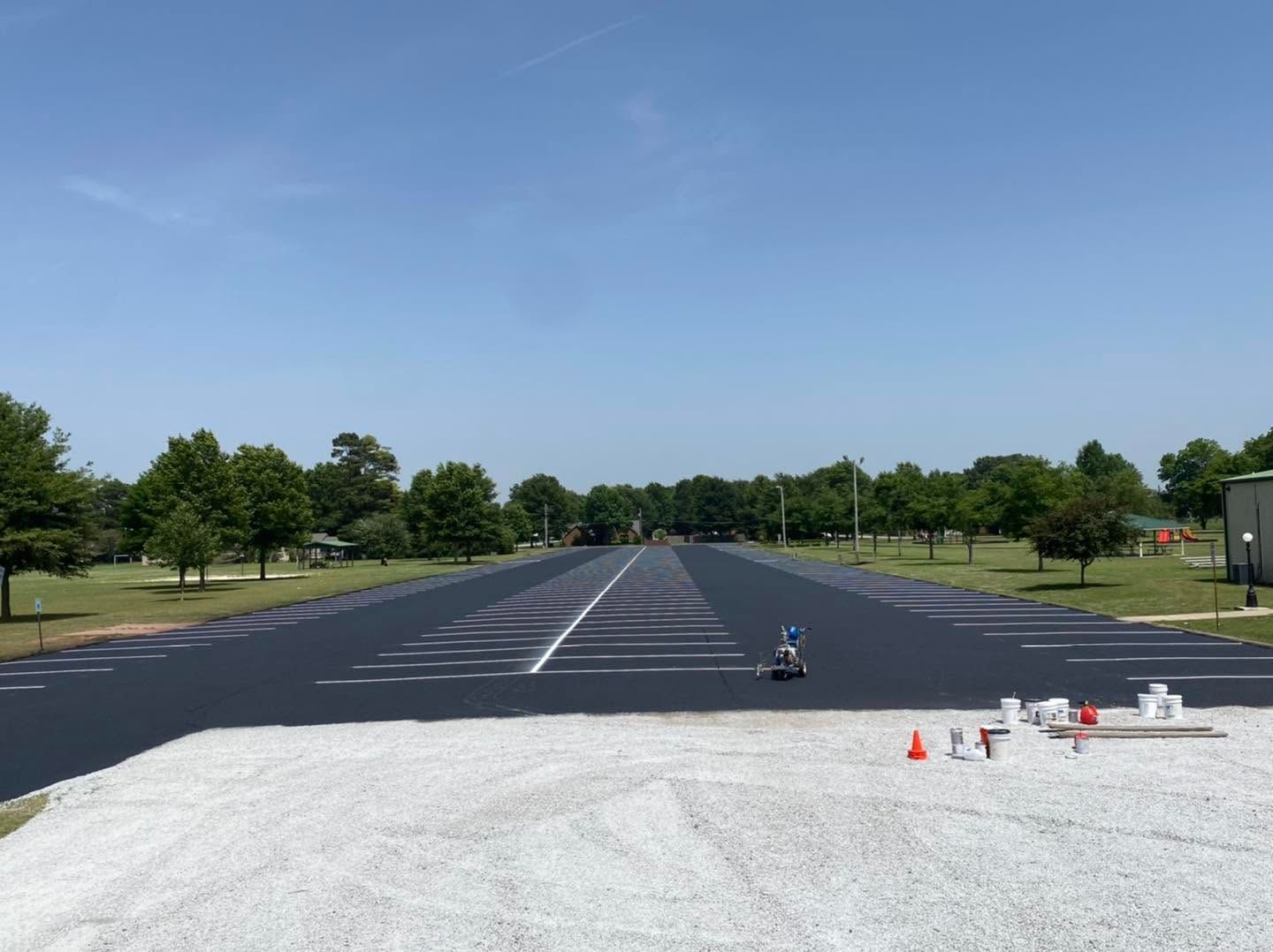 Wide paved road with white markings, trees on both sides, and cones and equipment in the foreground.