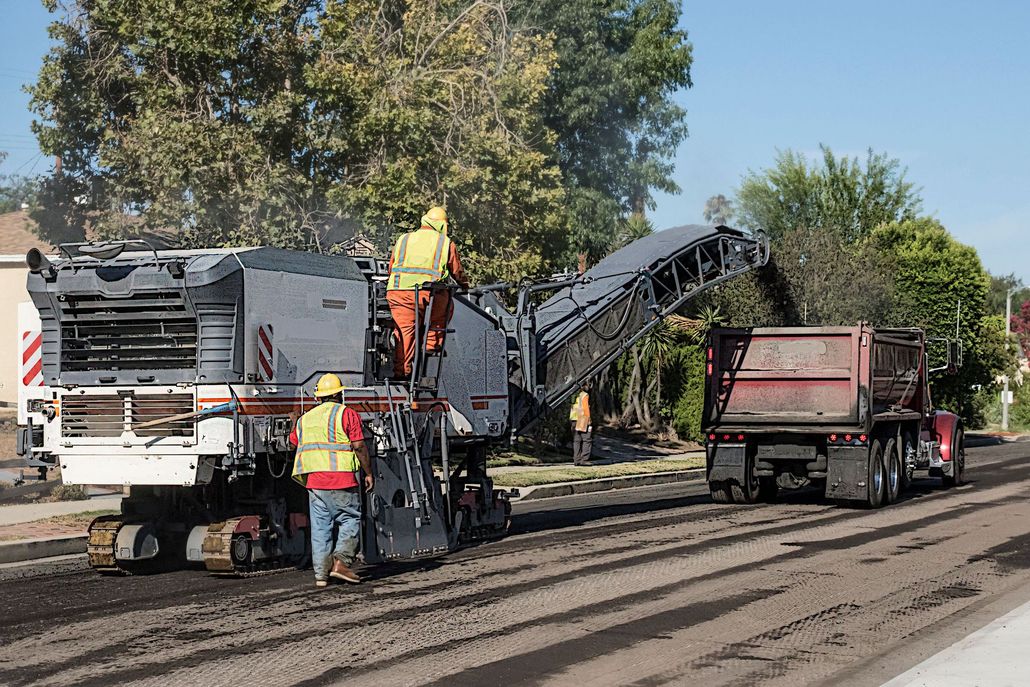 Road construction crew operating paving machine with dump truck on a freshly paved street