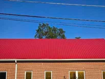 Red metal roof over a brick building with windows, under a blue sky with power lines and a tree.