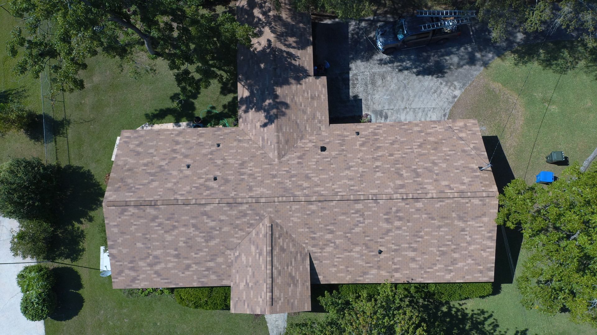 Overhead view of a house with a brown shingle roof, surrounded by green grass and trees.