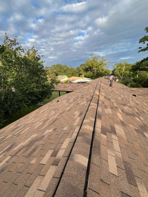 View of a brown shingled roof with a person working on it against a cloudy sky.