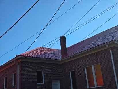 Brick building with red roof and chimney, power lines overhead, against a blue sky.