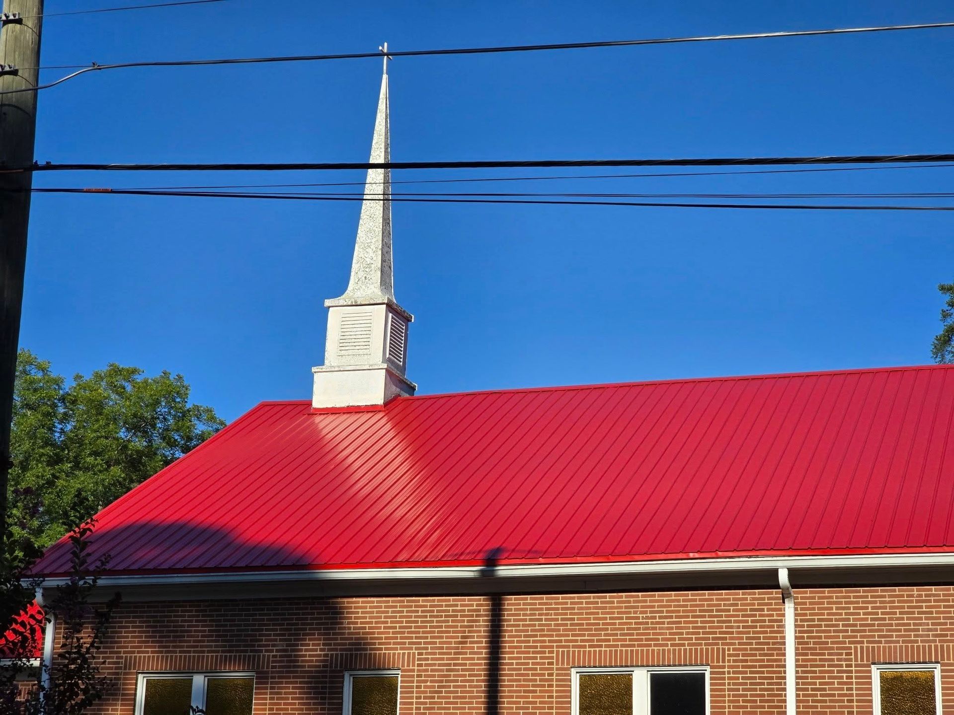 Church with a red metal roof and white steeple against a clear blue sky.