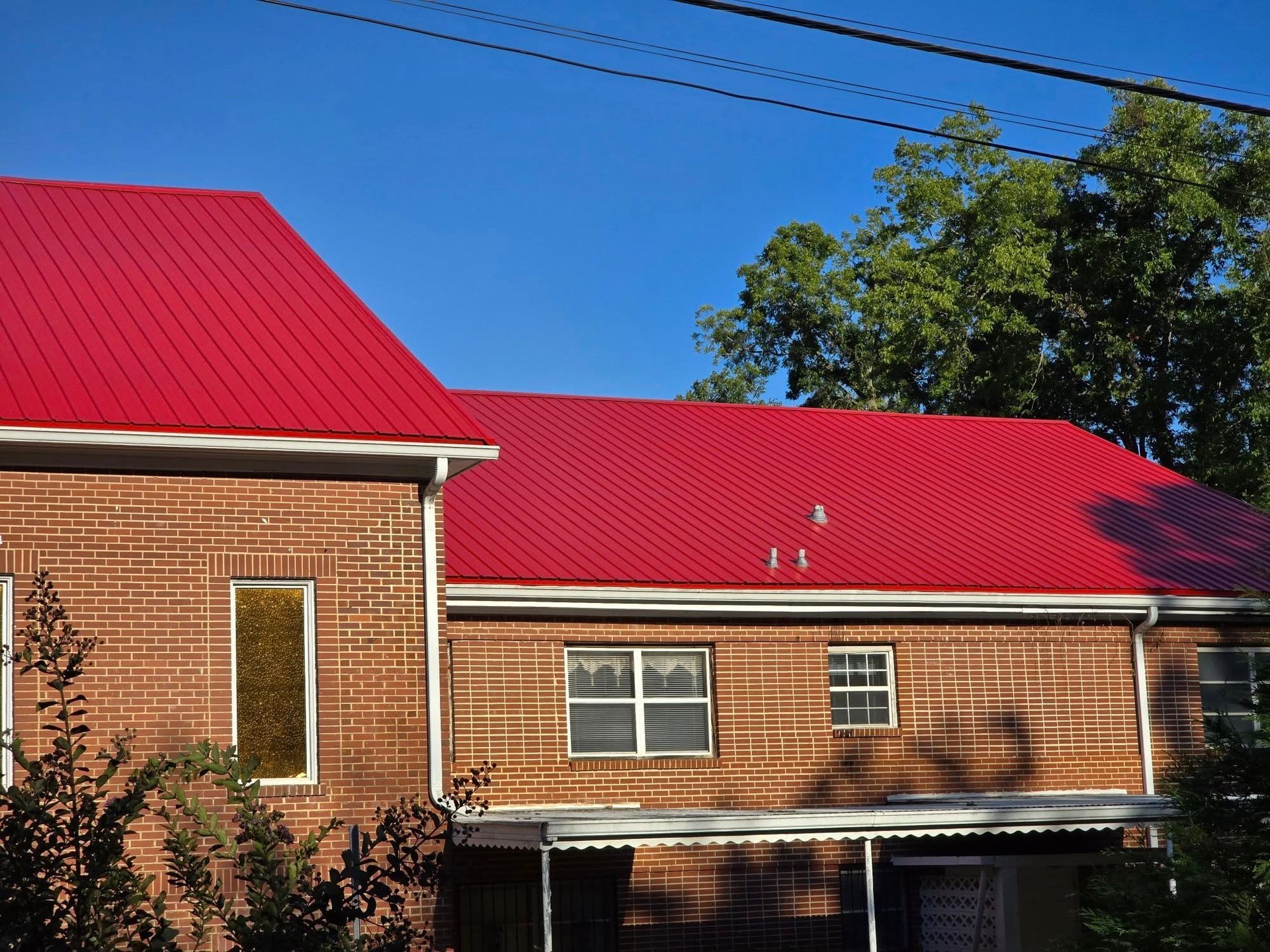 Brick house with bright red metal roof, white trim, and a blue sky.