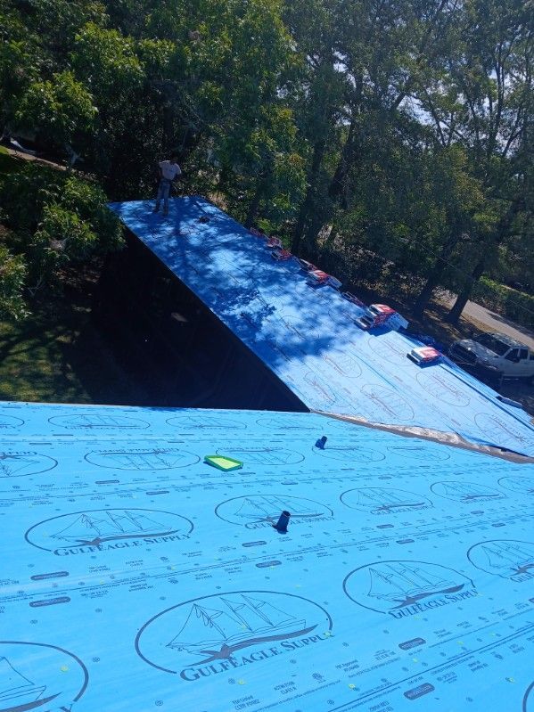 Roofing work in progress; blue underlayment, dark shingles, person on roof.