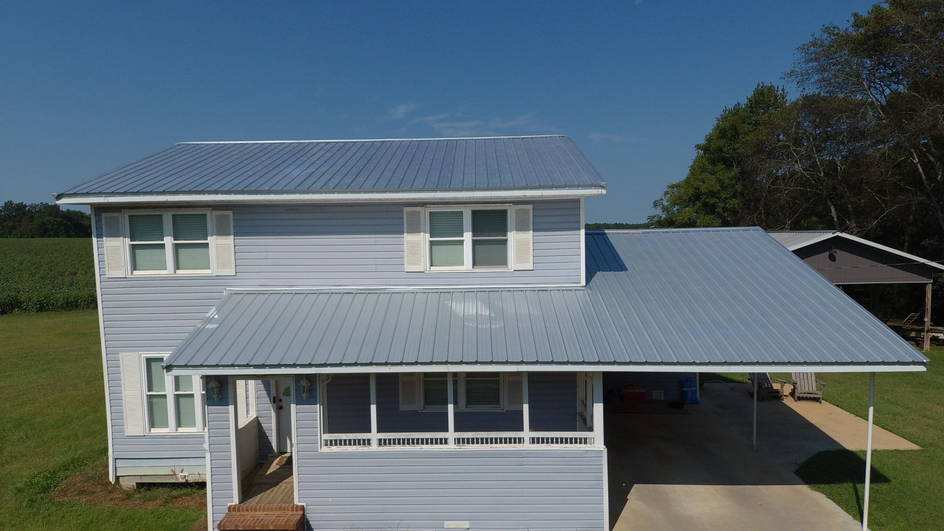 Blue two-story house with metal roof and carport on a sunny day.