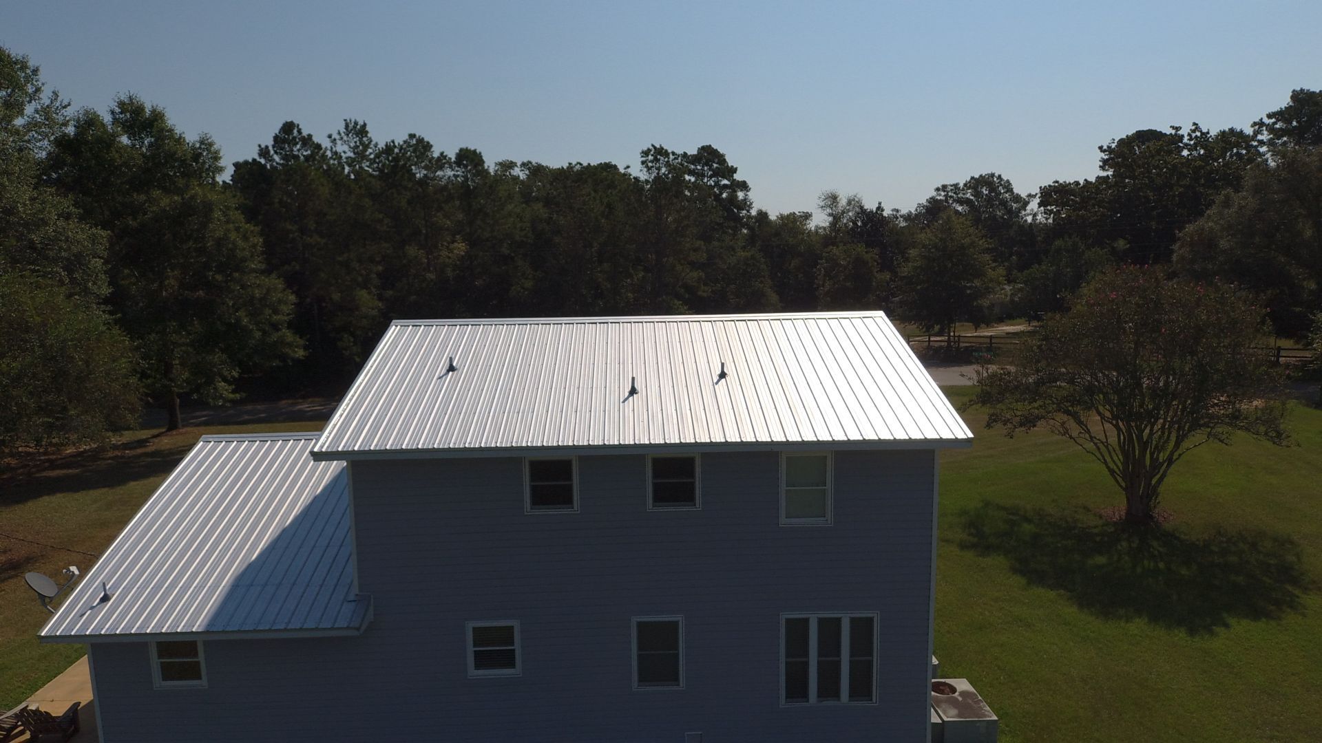 Blue house with silver metal roof, windows, and trees in the background under a blue sky.