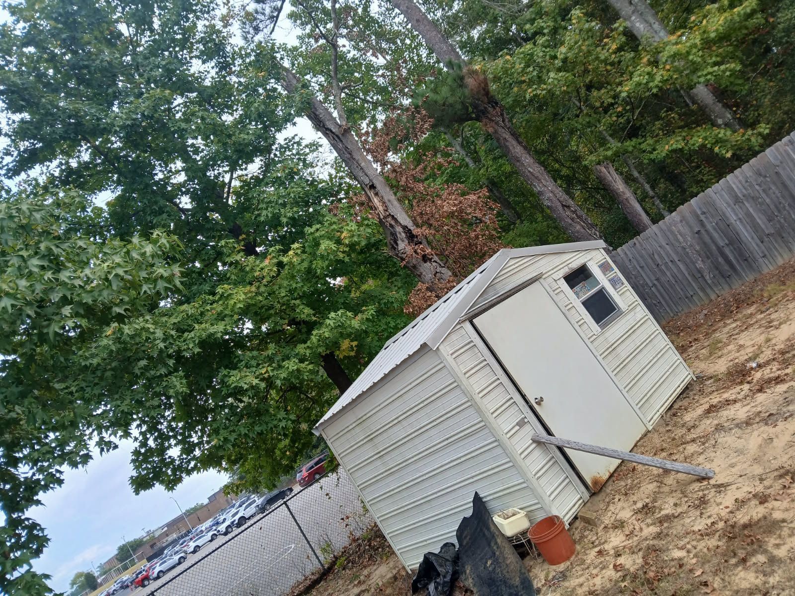 White storage shed in a yard, angled slightly, with trees and a fence in the background.