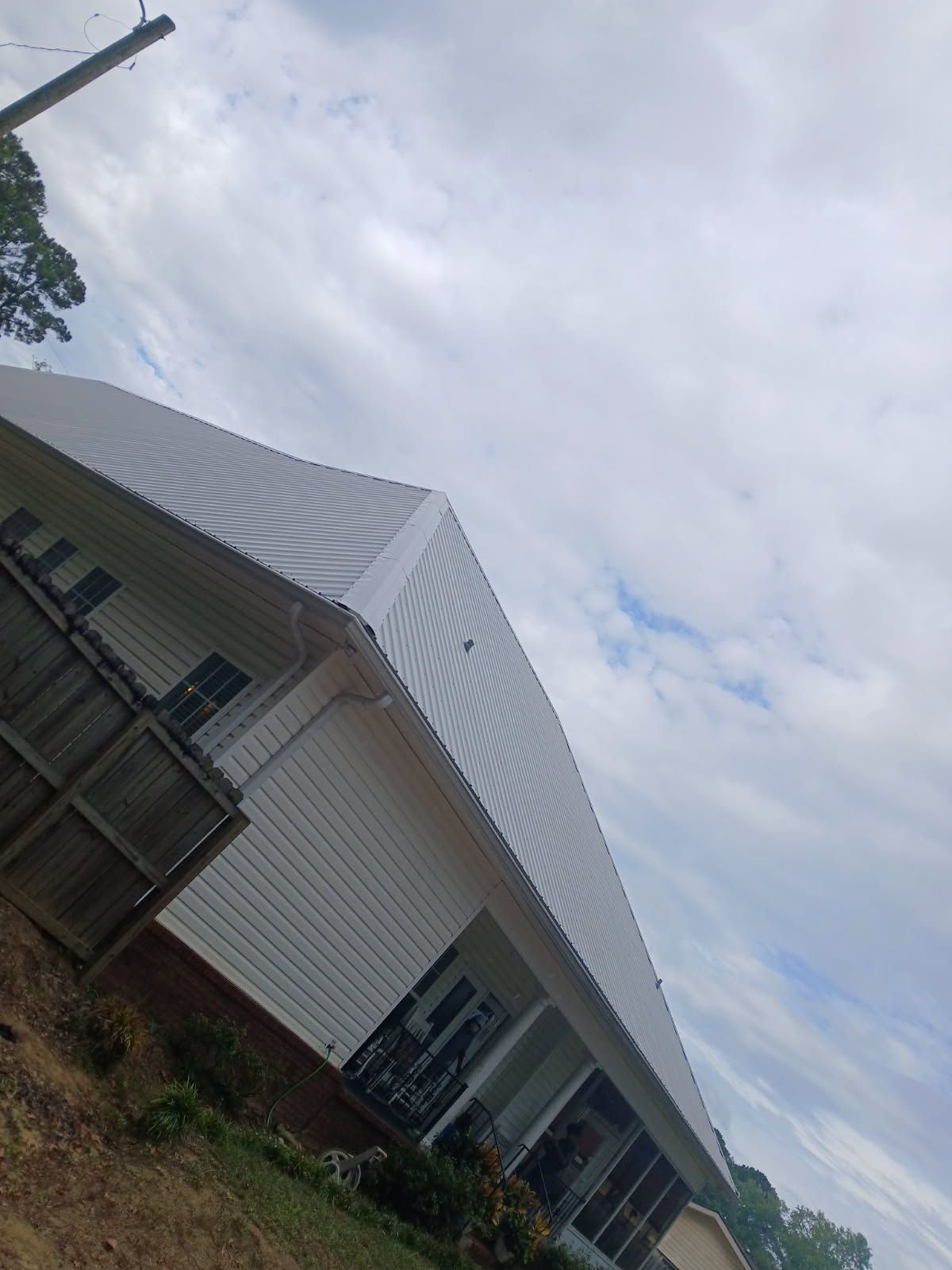 White building with light-colored siding, angled roof, and windows, set against a cloudy sky.