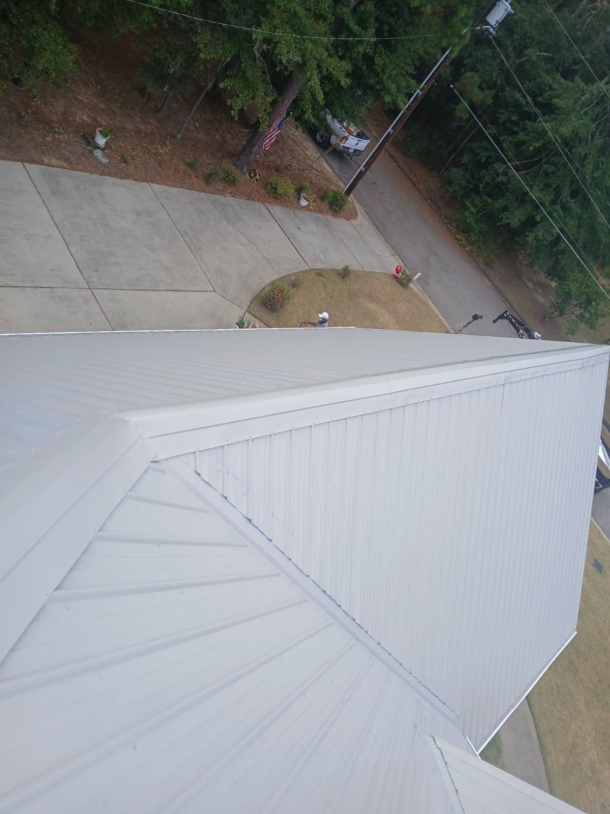 View from a roof of a gray metal building with a driveway and trees in the background.