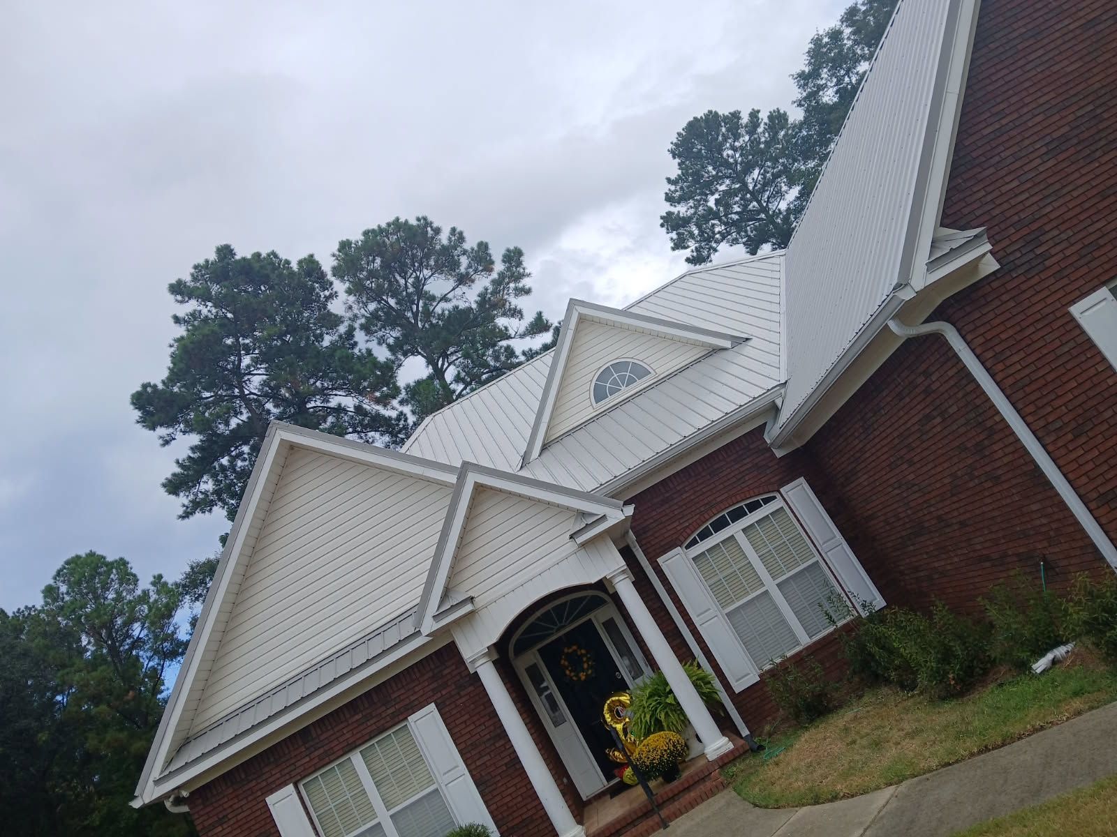 Brick house with white trim and metal roof, under a cloudy sky.