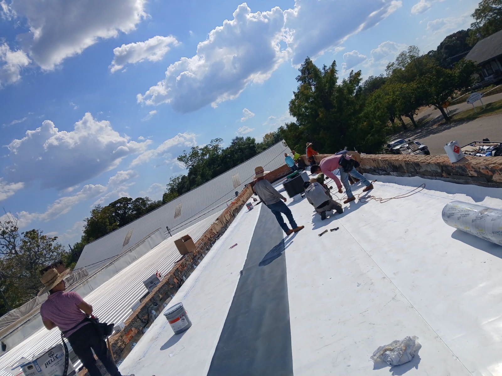 Workers installing a white roof on a building, blue sky with clouds overhead.