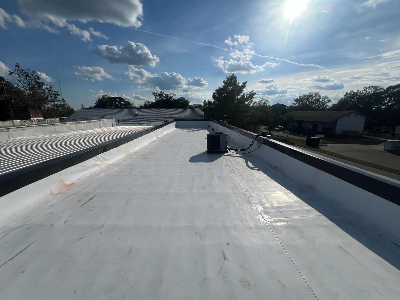 White flat commercial roof with black edges under a blue sky with sunlight.