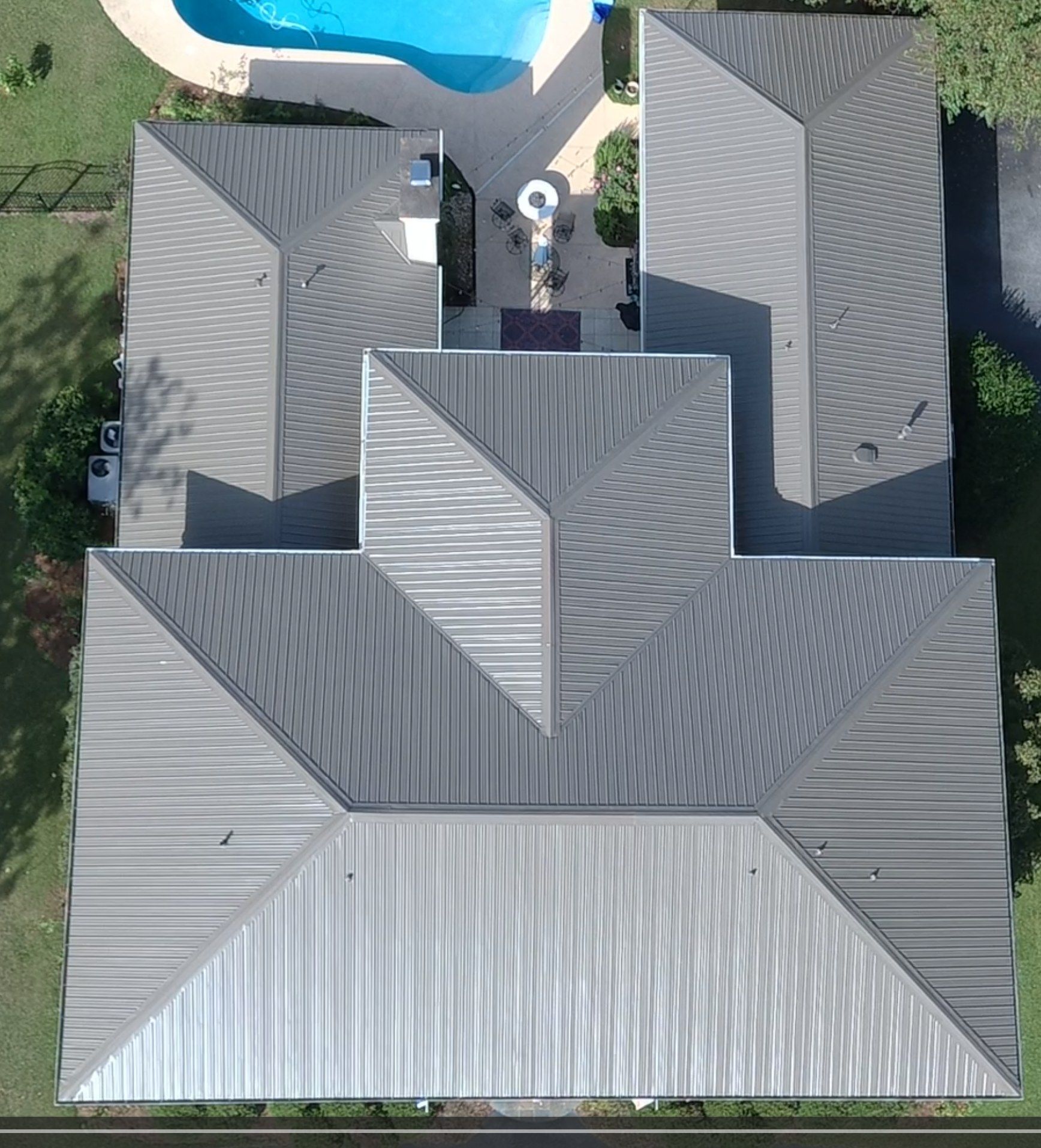 Aerial view of a gray roofed house with a pool in the background.