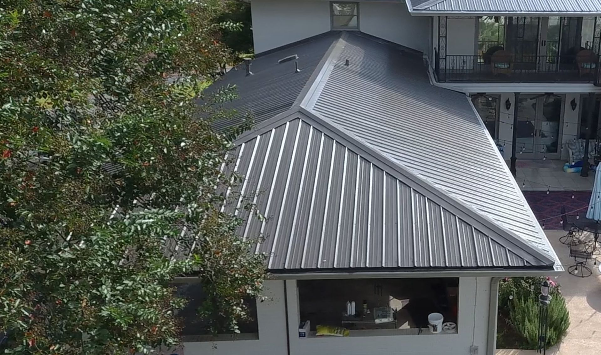 Black metal roof on a house, with trees on the left and a patio area on the right.