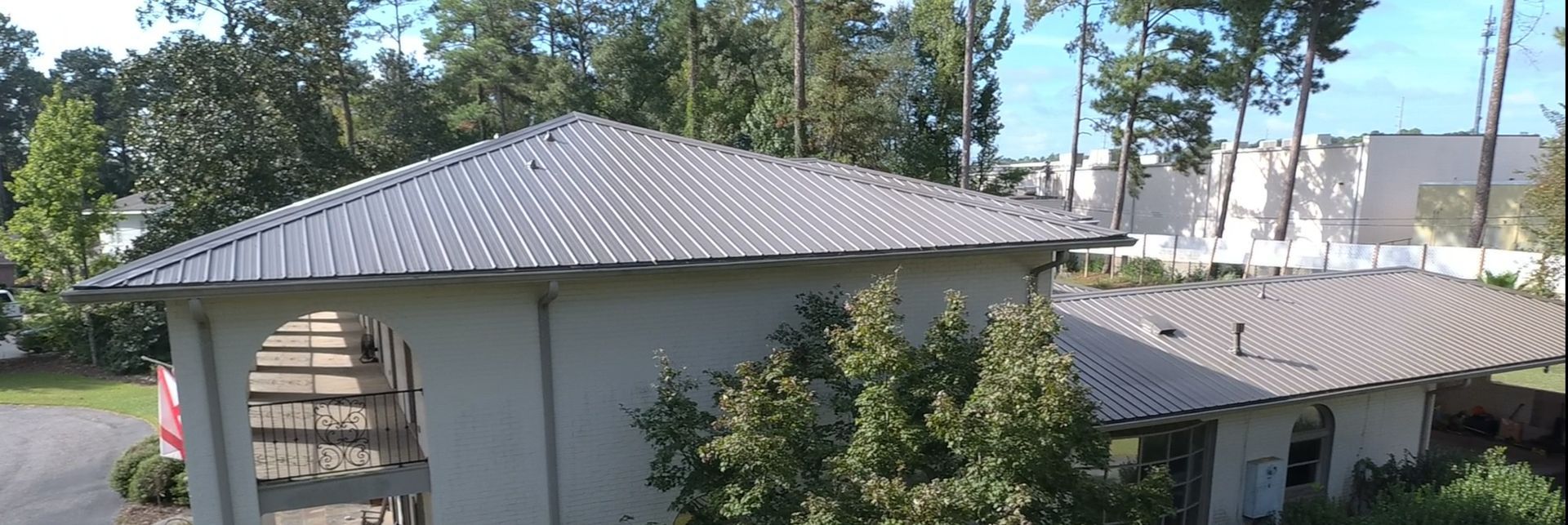 White building with corrugated metal roof surrounded by trees.