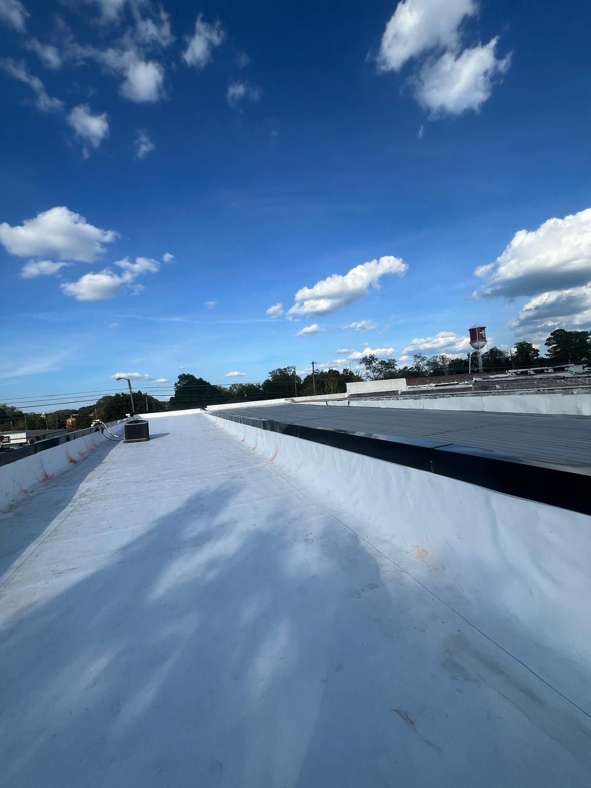 White flat roof under a blue sky with scattered clouds, distant trees and building.