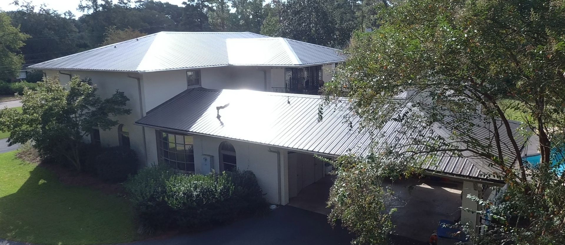 White, two-story house with a metal roof. Trees surround the house on a sunny day.