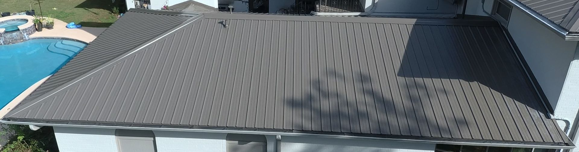 A gray roof of a house with a swimming pool visible in the distance.