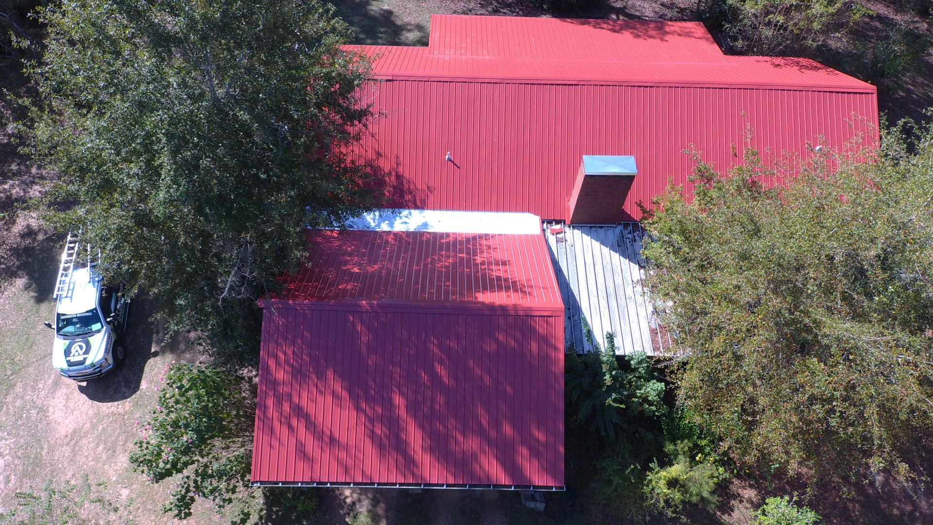 Overhead view of a red-roofed building partially obscured by green trees, a white truck parked to the side.