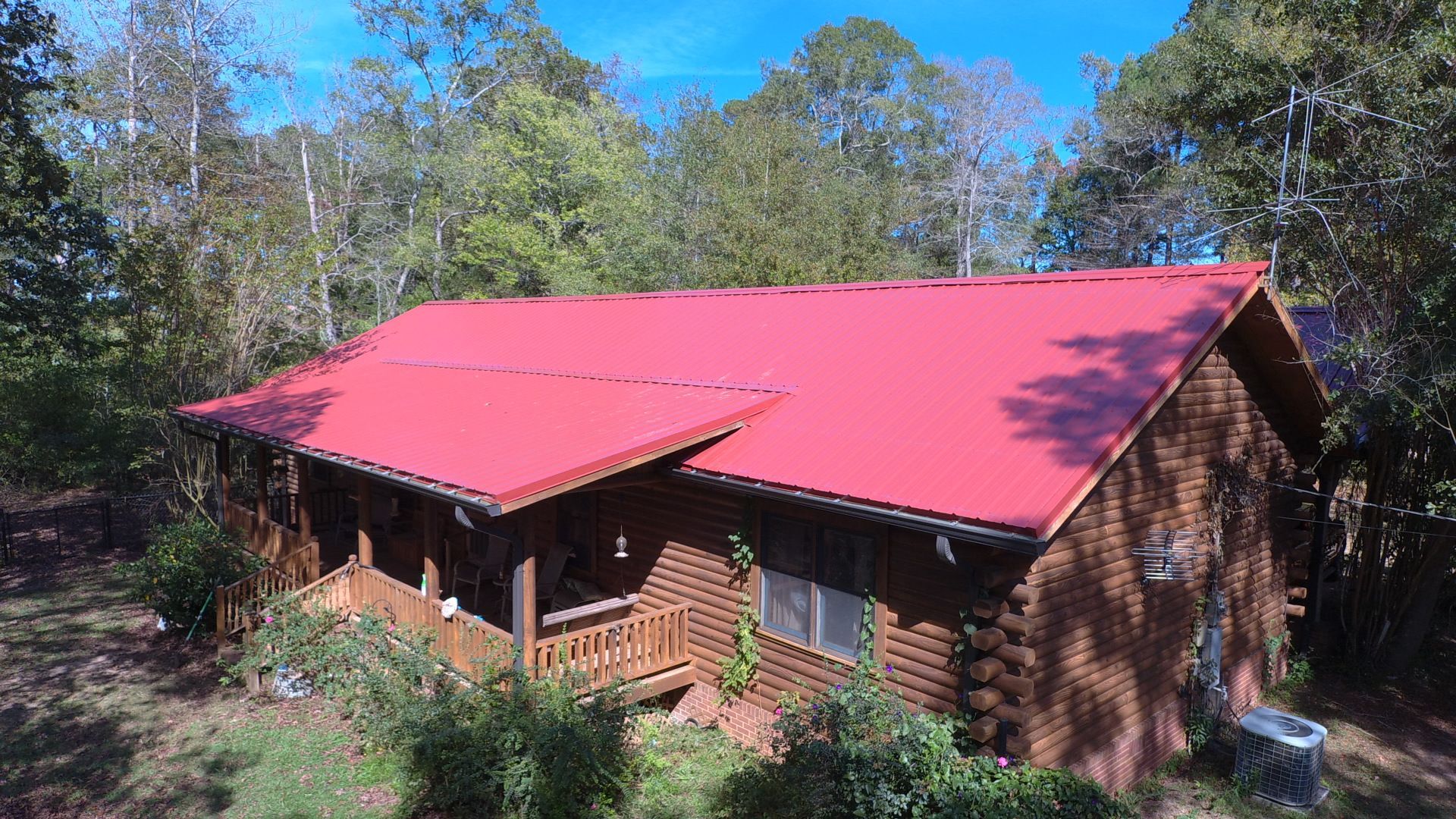 Log cabin with red metal roof surrounded by trees and foliage.