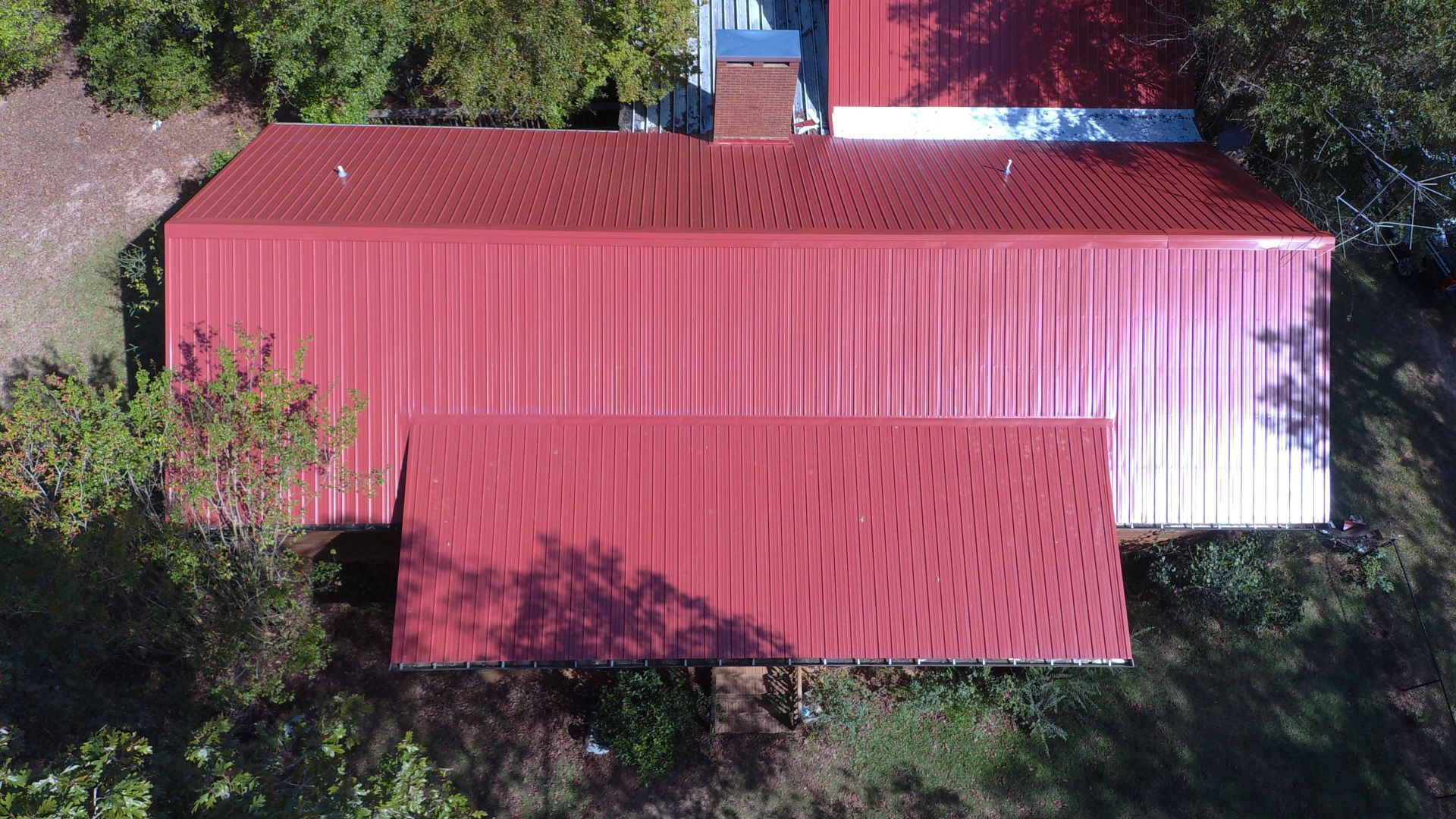 Overhead view of a red metal roof on a building, surrounded by green trees and foliage.