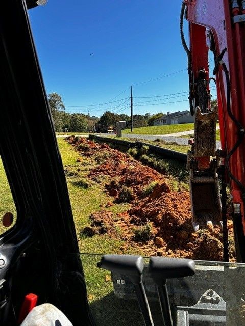 Excavator clearing red dirt along a roadside under a clear blue sky