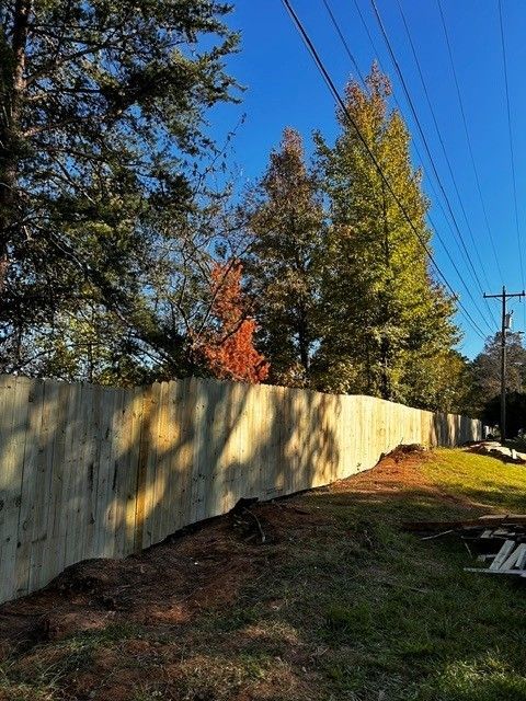 Sunlit wooden fence along a grassy yard with tall autumn trees and blue sky